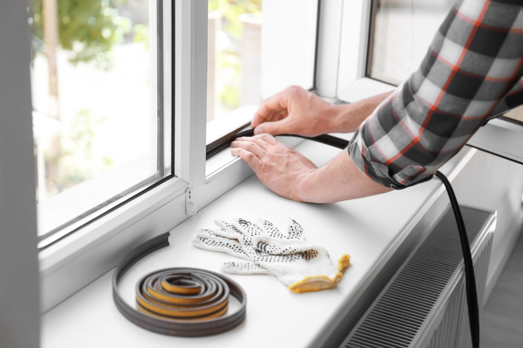 Young man putting sealing foam tape on window indoors